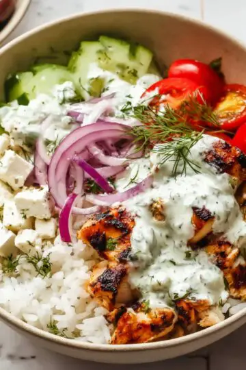 Greek Chicken Bowls Close up of a Greek chicken bowl with grilled chicken, white rice, cherry tomatoes, cucumber slices, red onion, Kalamata olives, feta cheese cubes, and creamy dill sauce, arranged in a beige bowl on a white tiled surface, bright natural lighting, high detail, overhead food photography style