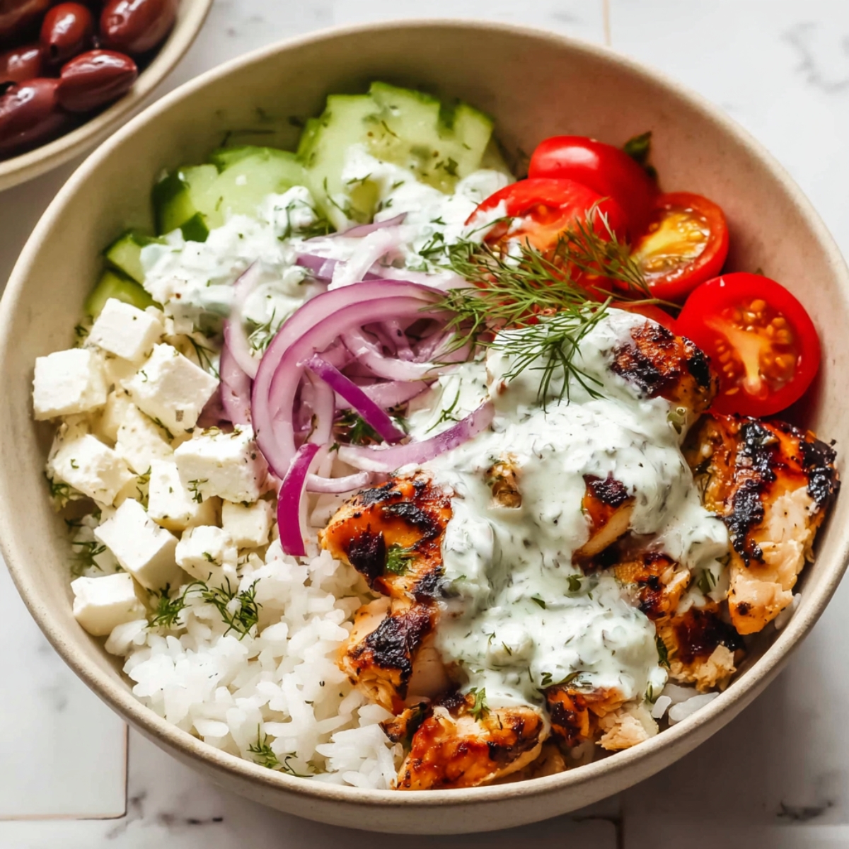 Greek Chicken Bowls Close up of a Greek chicken bowl with grilled chicken, white rice, cherry tomatoes, cucumber slices, red onion, Kalamata olives, feta cheese cubes, and creamy dill sauce, arranged in a beige bowl on a white tiled surface, bright natural lighting, high detail, overhead food photography style