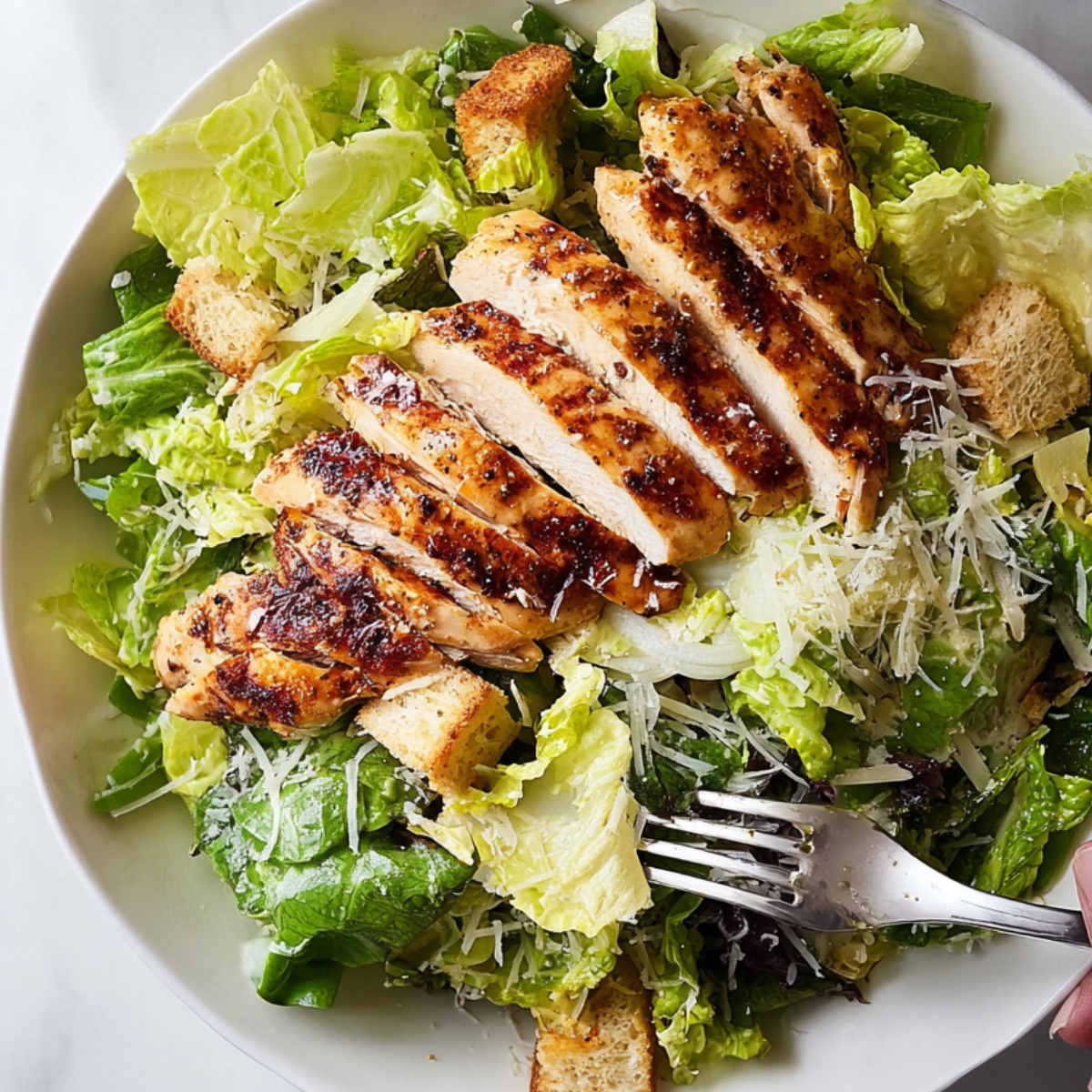 Sauteed Chicken Breasts Close up of sliced grilled chicken breast served on a fresh green salad with crisp romaine lettuce, crunchy croutons, and a sprinkle of shredded cheese. Hand holding a fork, ready to dig in, highlighting a healthy, protein-packed, and satisfying meal for lunch or dinner.