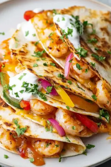 Sheet Pan Shrimp Fajitas Close up of freshly cooked shrimp quesadillas on a white plate, filled with plump shrimp, melted cheese, red and yellow bell peppers, and red onions, garnished with chopped cilantro, a dollop of sour cream, and a lime wedge on the side, vibrant colors, top-down food photography style, bright natural lighting highlighting textures and melted cheese.
