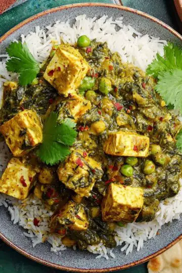 Tofu Spinach Green Pea Curry Close up of a plate of Palak Matar Tofu Curry served over fluffy white rice, garnished with fresh cilantro, with a side of naan and spices on a rustic green tiled surface, vibrant colors, top-down view, bright natural lighting, high-detail food photography, healthy Indian cuisine