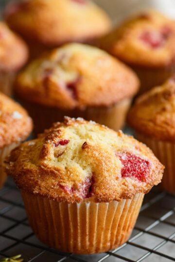 strawberry muffins A tempting close-up of homemade strawberry muffins, cooling after baking. The muffins are golden on the outside and soft on the inside, with juicy pieces of strawberries throughout. Captured on a wire rack with a soft kitchen backdrop, this image showcases the perfect texture and color of freshly baked muffins. These strawberry muffins are a simple yet delicious way to start the day or enjoy a sweet snack anytime.