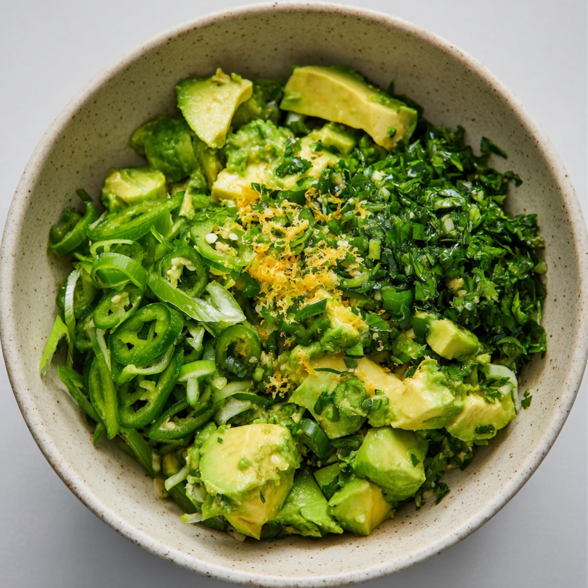 Close up of a colorful and fresh avocado herb mixture, combining creamy avocado cubes, chopped parsley, sliced scallions, spicy green chili, and zesty lemon. Captured in natural light in a rustic ceramic bowl, this image showcases the textures, vibrant colors, and freshness of wholesome ingredients, perfect for healthy recipe blogs or social media posts.