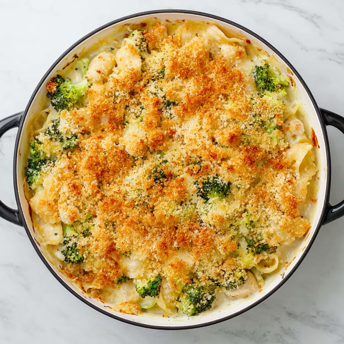 Close up of baked chicken and broccoli pasta casserole in a round white baking dish with black handles, topped with golden-brown breadcrumbs, melted cheese, and crispy edges, sitting on a white marble countertop, home-cooked comfort food, high detail texture, overhead view.