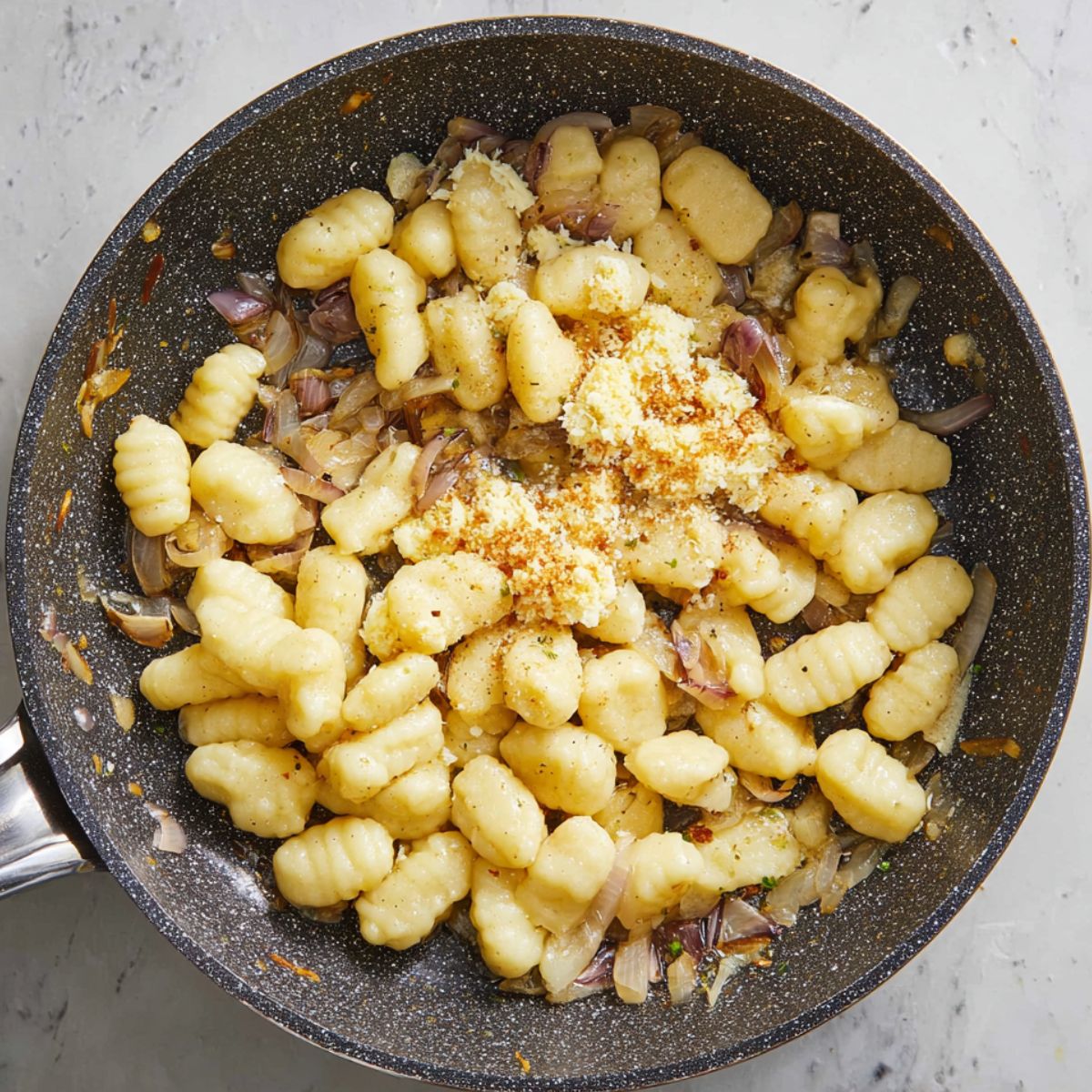 Close up of uncooked gnocchi in a skillet with sautéed onions and seasonings, topped with grated cheese, natural overhead lighting, textured non-stick pan, high detail, cozy home cooking scene, rustic and appetizing