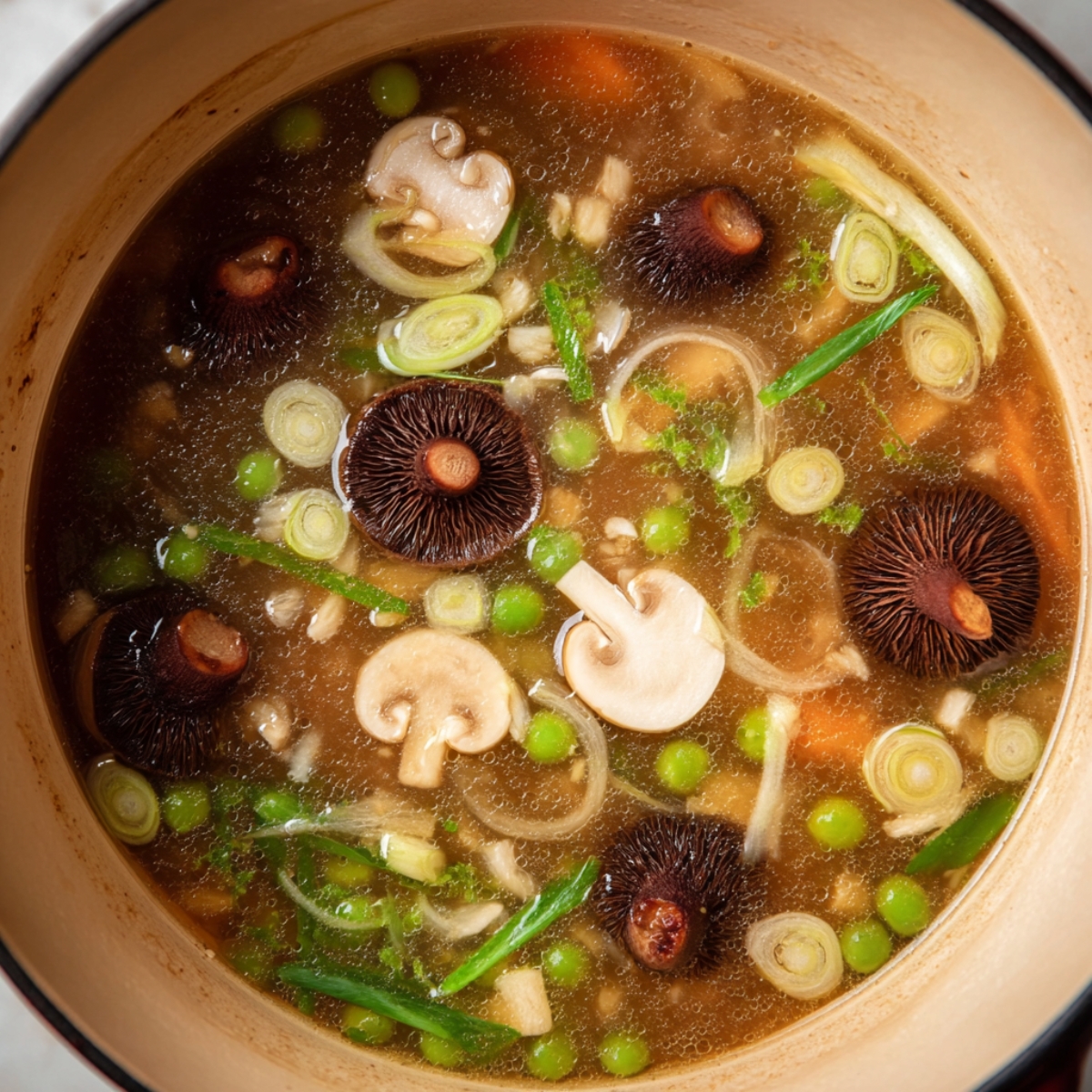 A cozy, inviting bowl of mushroom miso soup captured in rich detail, showing plump shiitake mushrooms, bright green onions, and thinly sliced vegetables floating in a steaming, aromatic broth. The natural lighting emphasizes the textures and depth of flavor, making it an ideal representation of healthy, homemade Japanese-inspired comfort food.