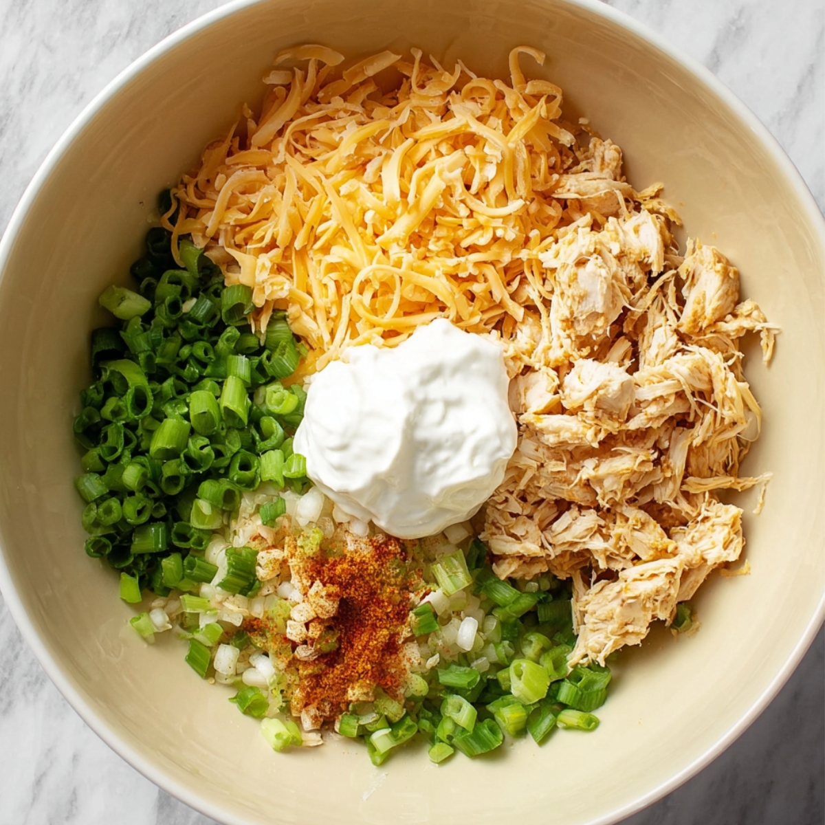 Close-up of a bowl with shredded cheese, diced chicken, green onions, and spices, ready to be mixed for a flavorful enchilada filling.