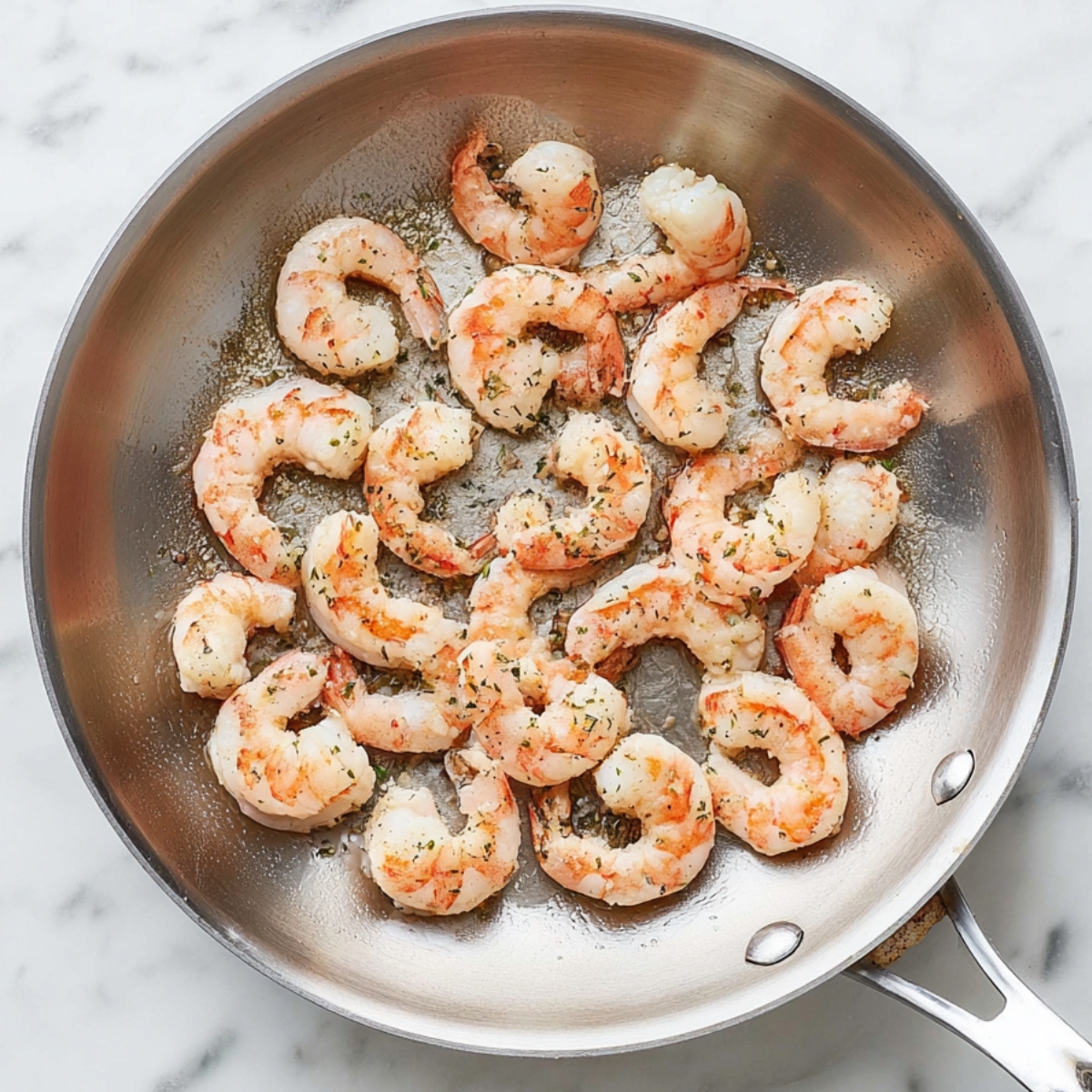 Close up of cooked shrimp in a stainless steel frying pan on a white marble countertop, highlighting the pink and white textures of the shrimp, natural lighting, food photography, top-down view, high detail, appetizing presentation.
