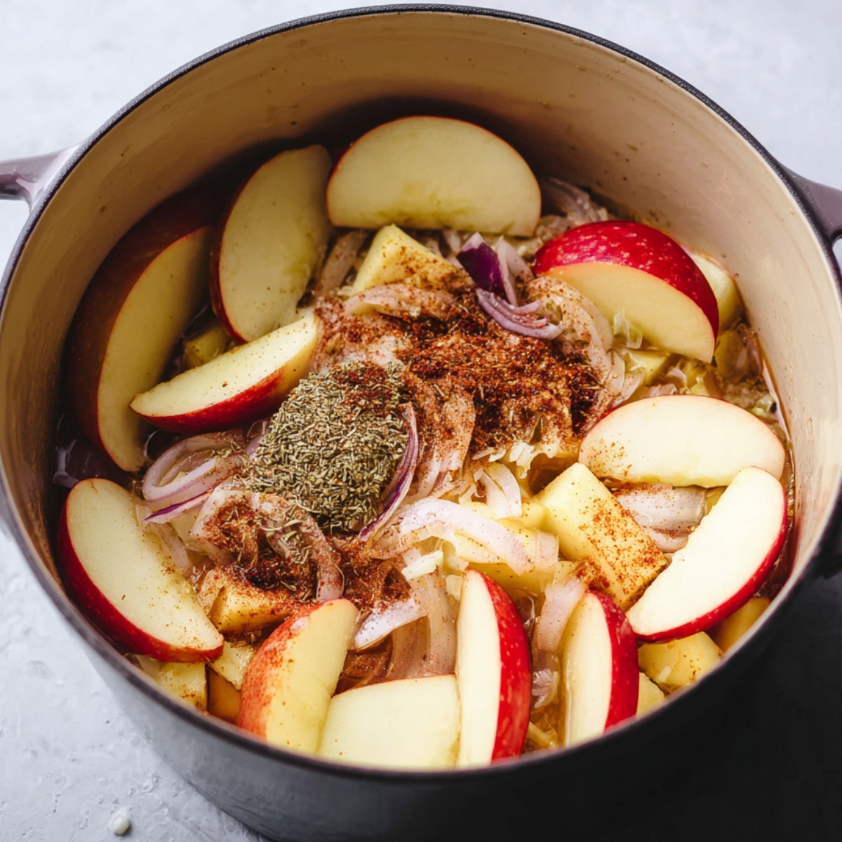 Close up of a Dutch oven filled with sliced apples, onions, minced garlic, brown sugar, mustard, and spices, ready to be cooked with pork and sauerkraut, showing vibrant textures and colors, top-down view, bright natural lighting, high detail, appetizing food photography style.