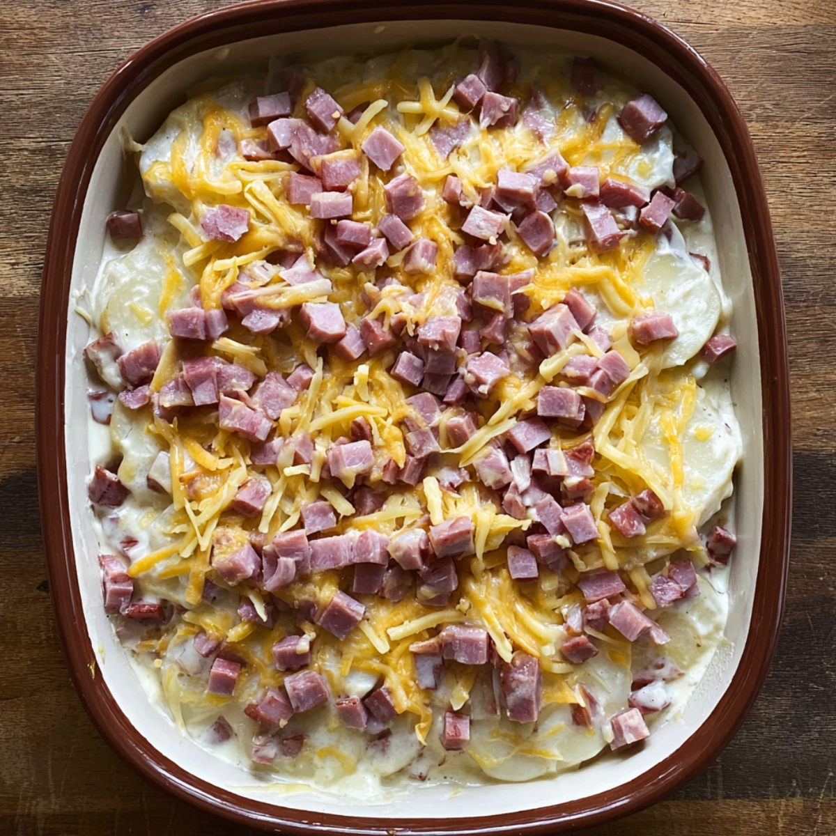 Close up of a plated serving of baked scalloped potatoes and ham, melted golden cheddar cheese on top, creamy layers with diced ham, garnished with fresh parsley, fork beside the portion, warm and inviting, high-detail food photography, natural lighting