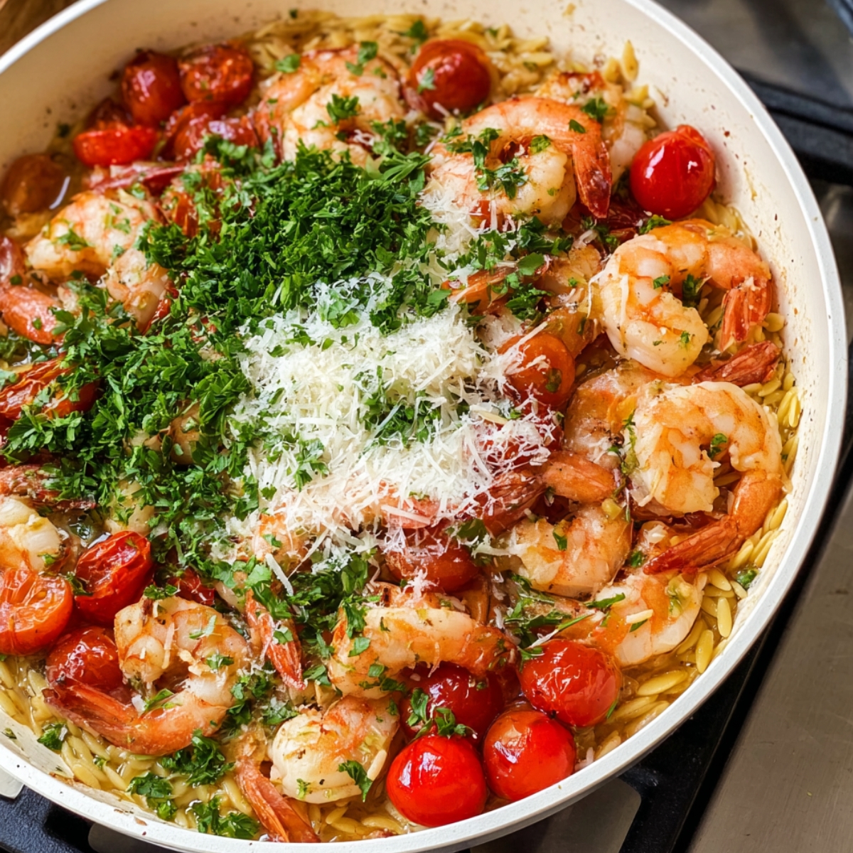 Close up of a white skillet filled with cooked shrimp, halved cherry tomatoes, grated Parmesan cheese, and fresh chopped parsley over orzo, vibrant colors, rich textures, warm kitchen lighting, top-down view, culinary food photography style, high detail, appetizing presentation