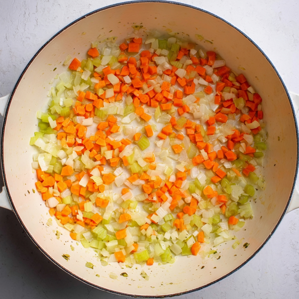 Close up of a creamy orange bean and vegetable soup in a simple white bowl, garnished with fresh parsley leaves and served with a bright lemon wedge on the side. The soup is thick and rich, with visible chunks of carrots, celery, and white beans, sprinkled lightly with cracked black pepper and red pepper flakes. The bowl sits on a matching white plate with a silver spoon resting beside it, surrounded by scattered parsley leaves for a natural, cozy presentation. The scene is lit with soft natural daylight from above, emphasizing the vibrant colors and creamy texture of the soup, creating a warm, inviting atmosphere perfect for comfort food photography.