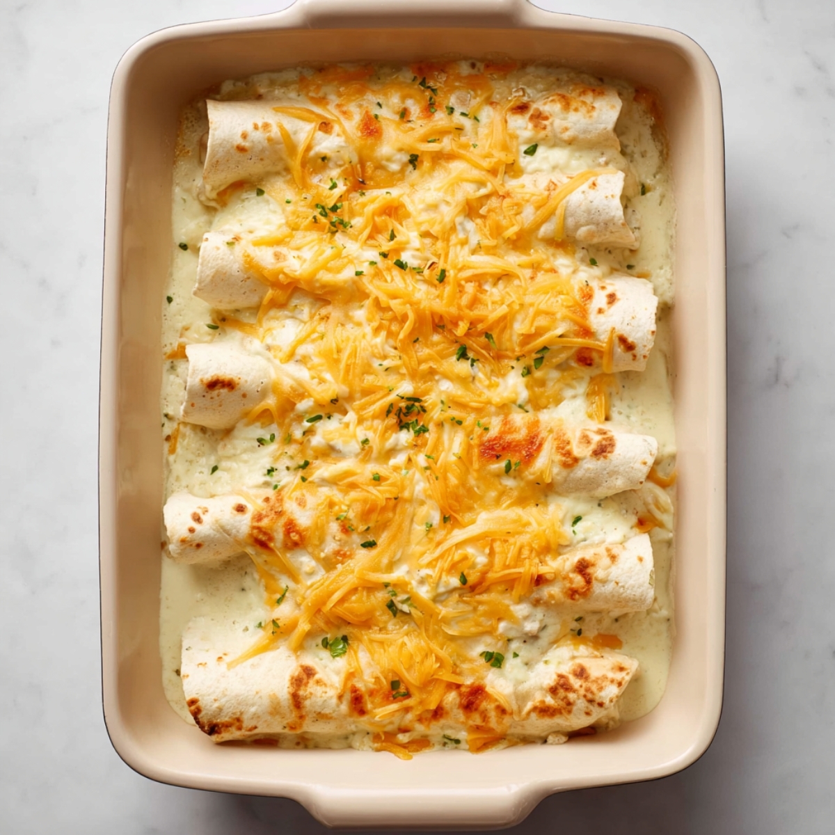 Indulge in this deliciously cheesy white chicken enchilada topped with a rich creamy sauce and a blend of shredded cheddar and mozzarella. Close up view highlights the gooey melted cheese, tender chicken filling, and vibrant garnishes of cilantro and green onions. Perfect for a hearty dinner, meal prep, or even entertaining guests with a dish that looks as good as it tastes.