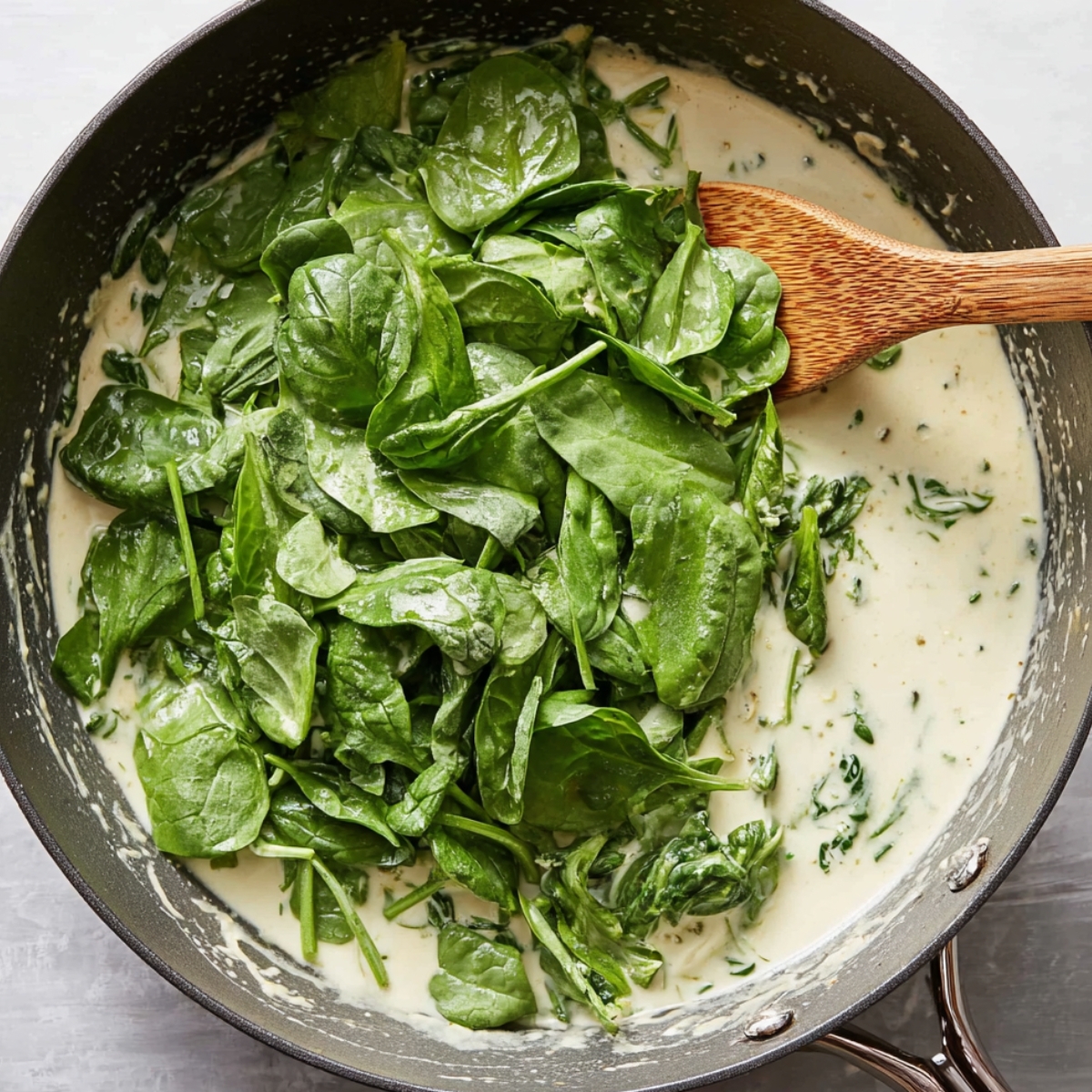 Close up of fresh spinach leaves being stirred into a creamy sauce, ready to wilt and infuse the dish with flavor.